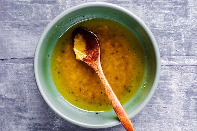 A bowl of olive oil and mustard dressing with a small wooden spoon.