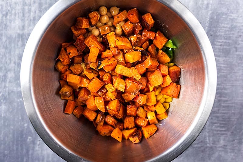 Cooked cubes of sweet potato in a bowl with salad ingredients and a dressing.