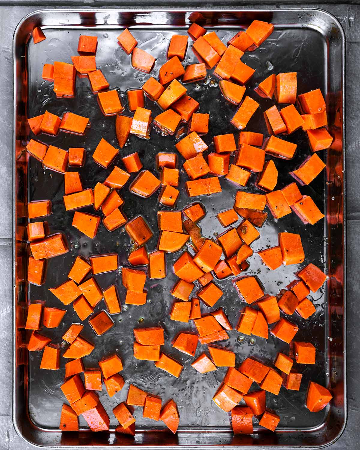 A large baking tray covered with cubes of sweet potato.