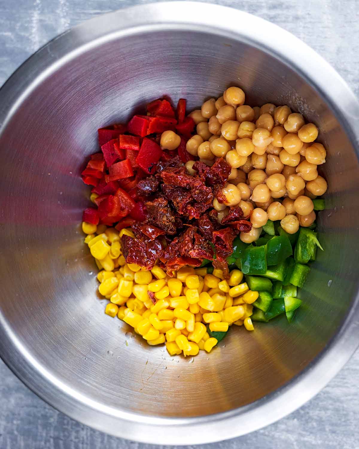 A mixing bowl containing chickpeas, chopped peppers, sun dried tomatoes and sweetcorn.