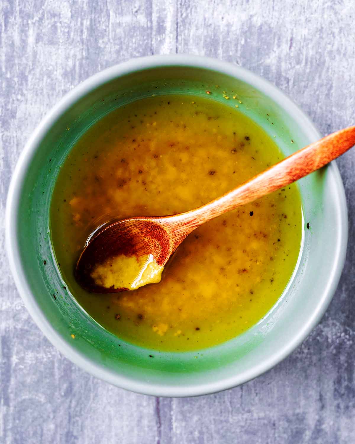 A bowl of olive oil and mustard dressing with a small wooden spoon.