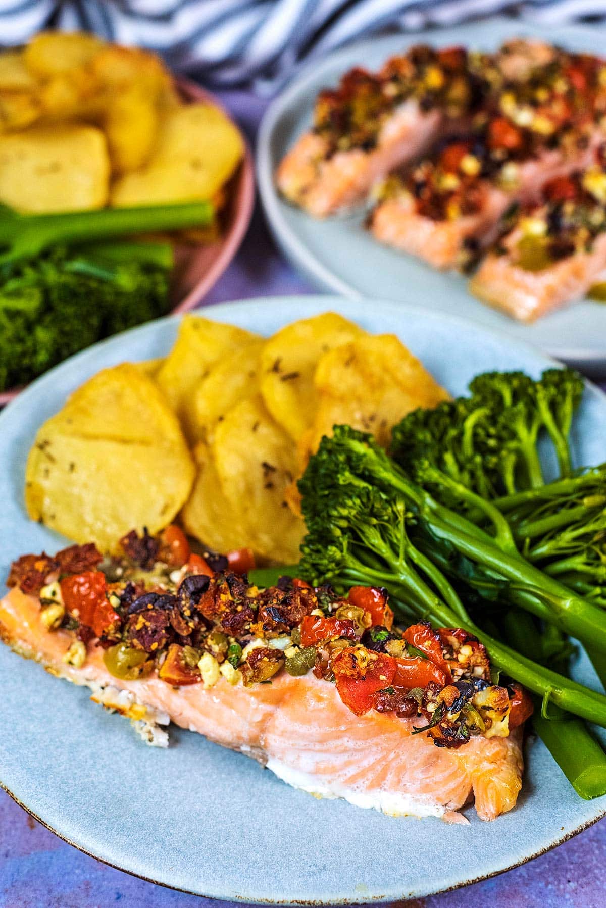 A plate of salmon, broccoli and potatoes in front of another plate of salmon.
