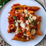 A plate of penne arrabiata topped with chopped herbs and Parmesan shavings