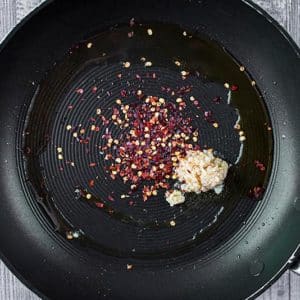 A frying pan with minced garlic and chili flakes cooking in it