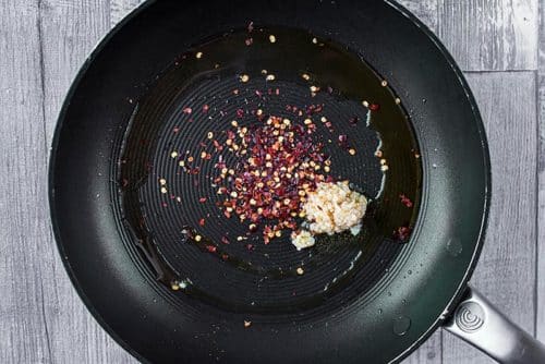 A frying pan with minced garlic and chili flakes cooking in it