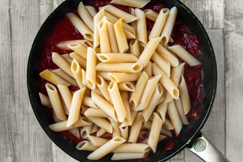 Cooked pasta in a frying pan on top of a tomato souce