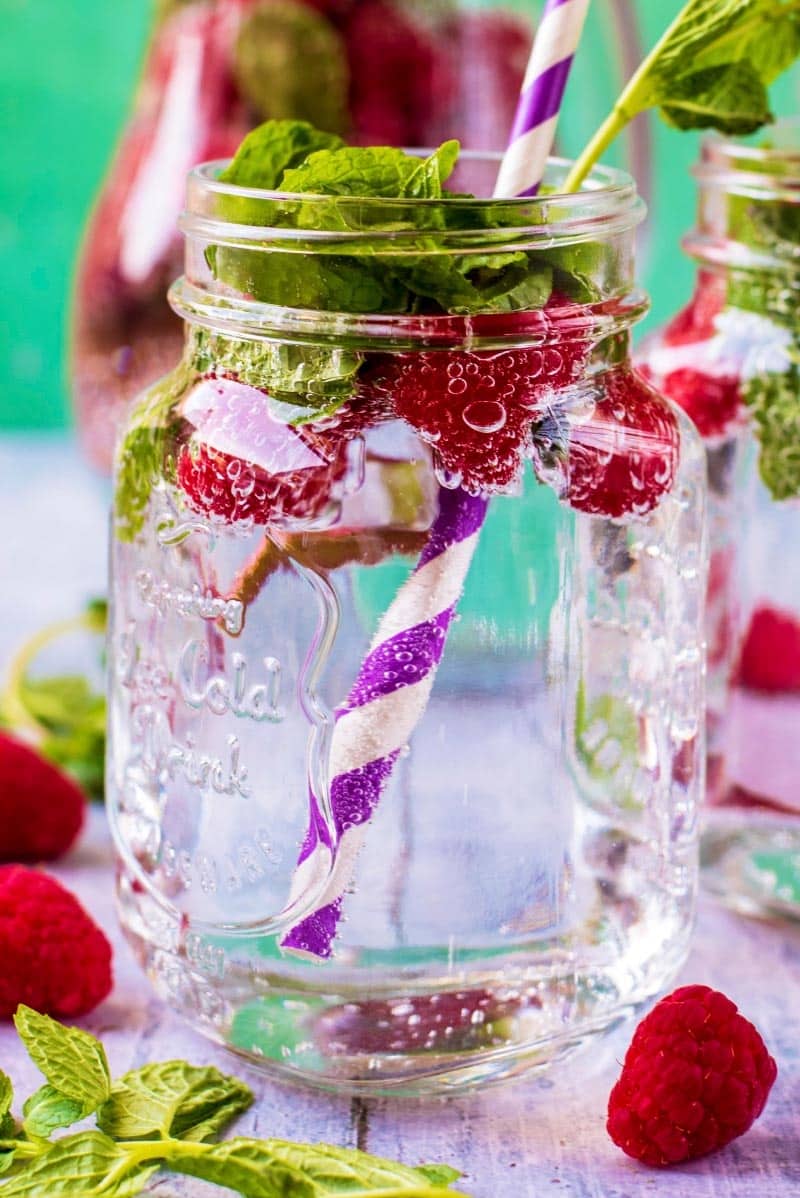 A mason jar filled with raspberry sparkling water with a striped straw