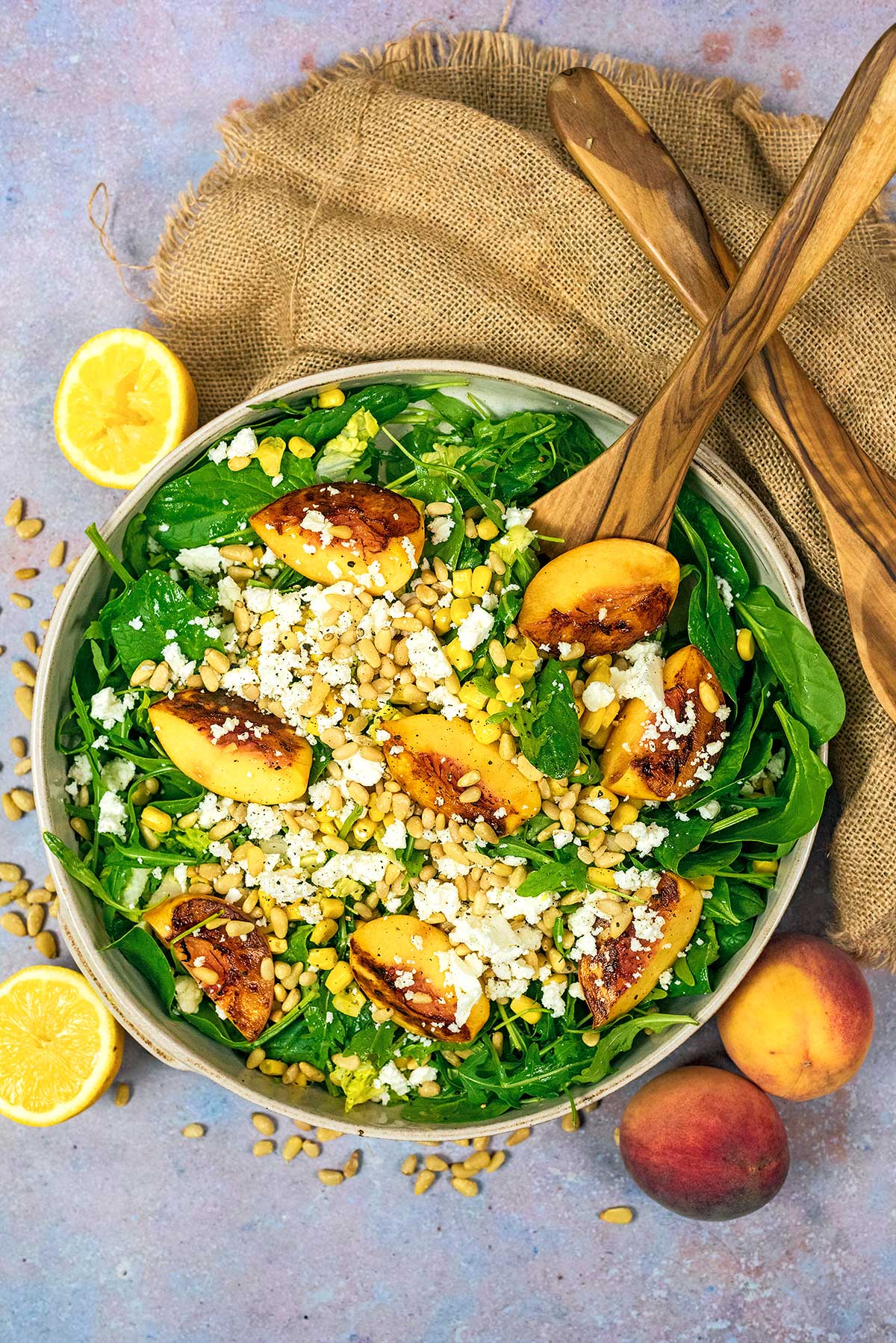 A large bowl of salad surrouded py peaches and lemons.