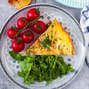 A slice of Spanish omelette on a plate with vine tomatoes and green salad leaves