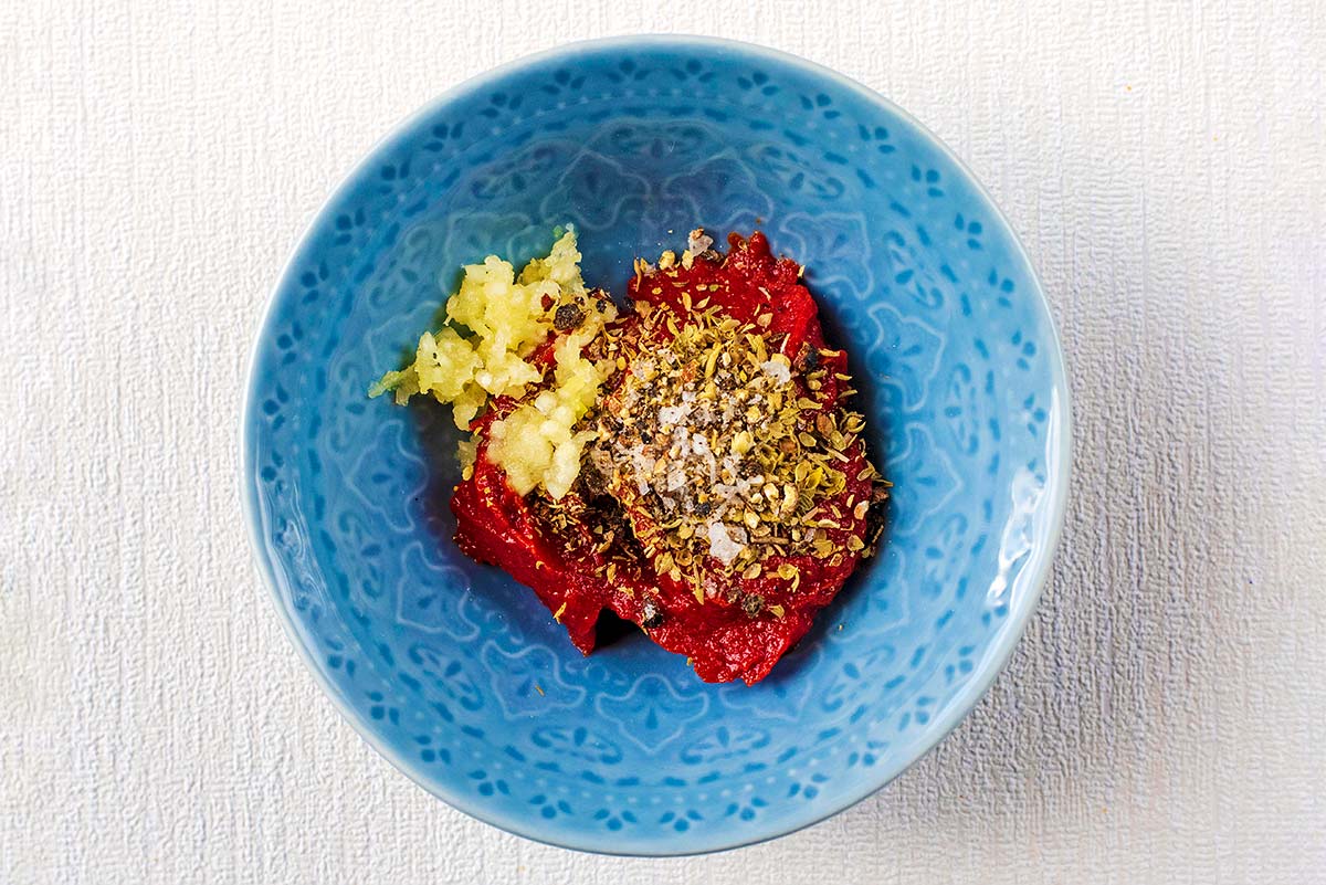 A small blue bowl with tomato puree, crushed garlic and dried oregano in it.