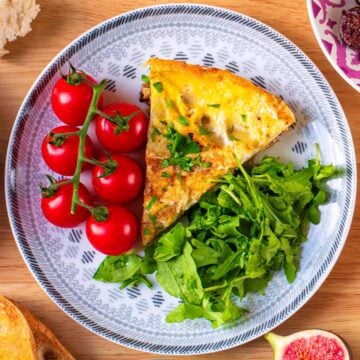 A slice of Spanish omelette on a plate with vine tomatoes and green salad leaves