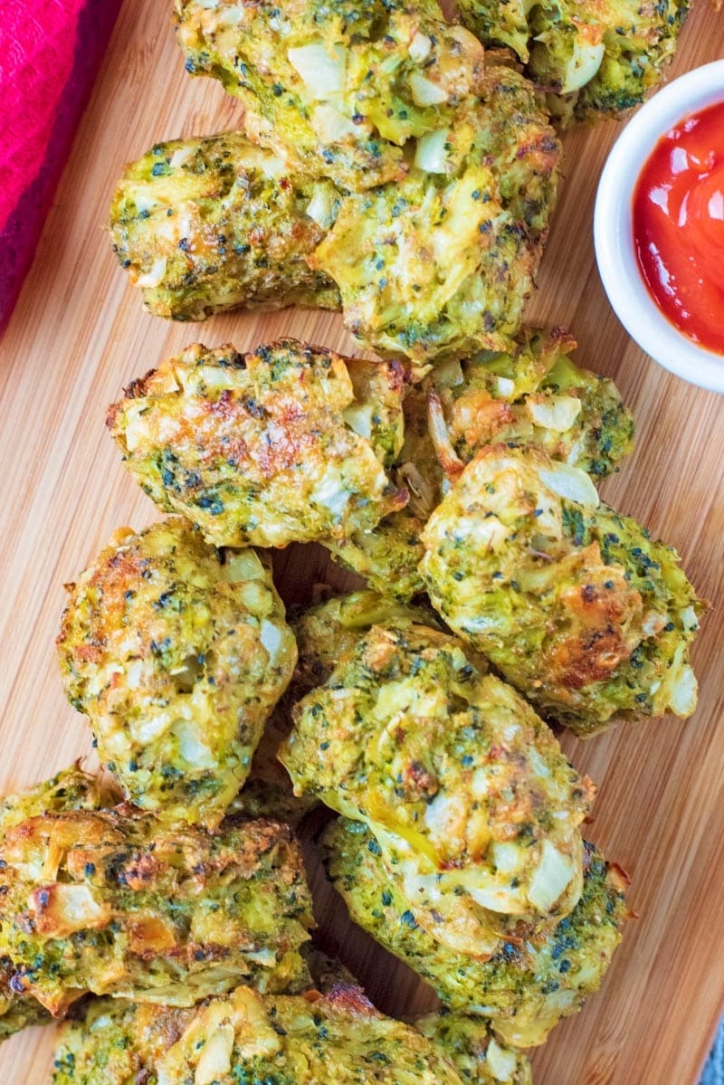 Baked Broccoli Bites stacked on a board with tomato sauce. A red towel next to them.
