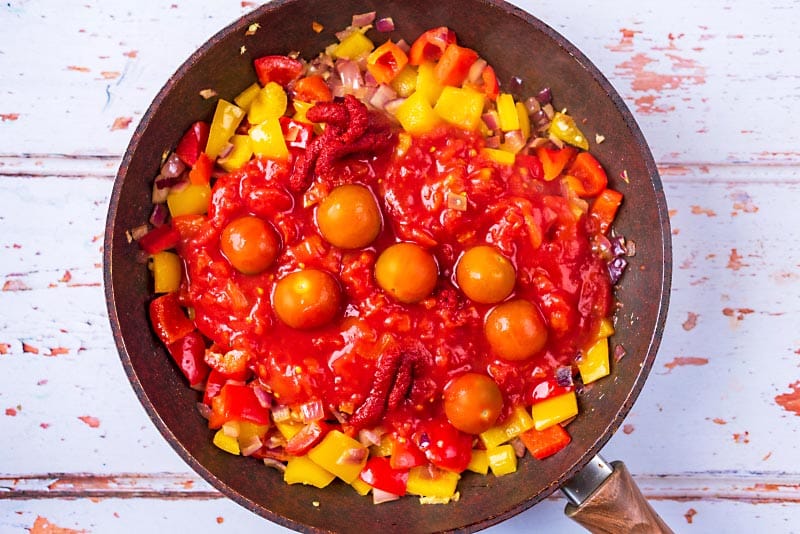 A frying pan with chopped vegetables, chopped tomatoes and cherry tomatoes.