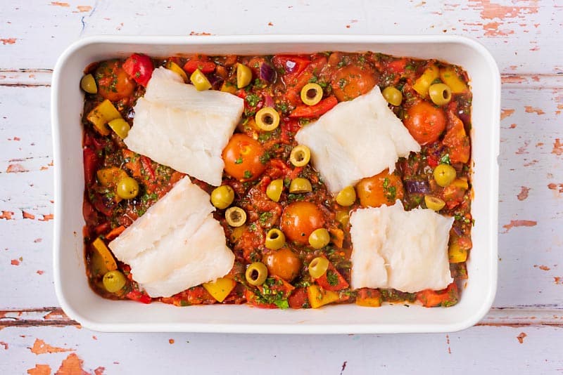 A baking dish with a tomato vegetable sauce and white fish fillets.