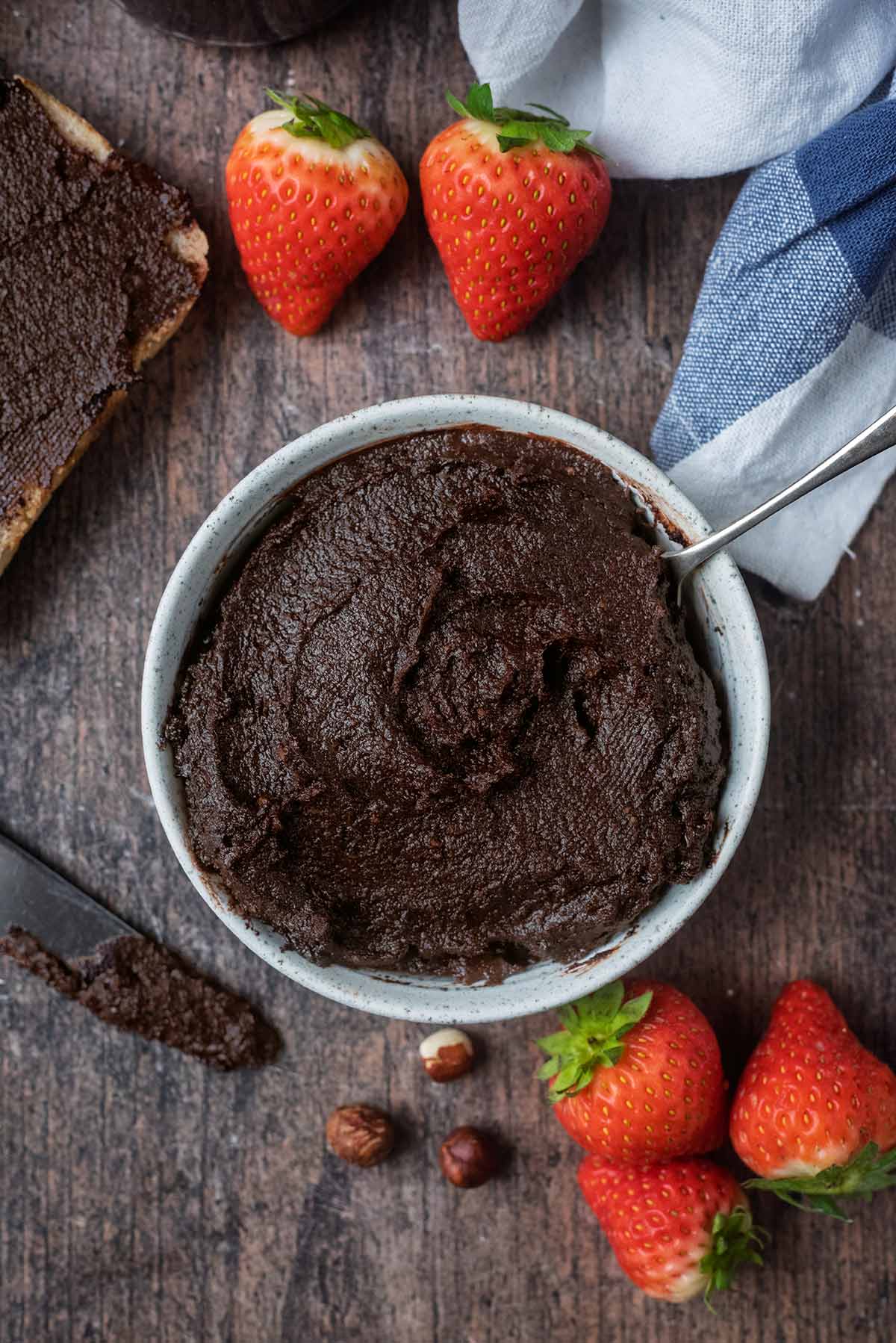A bowl of chocolate nutella next to a towel and some strawberries.