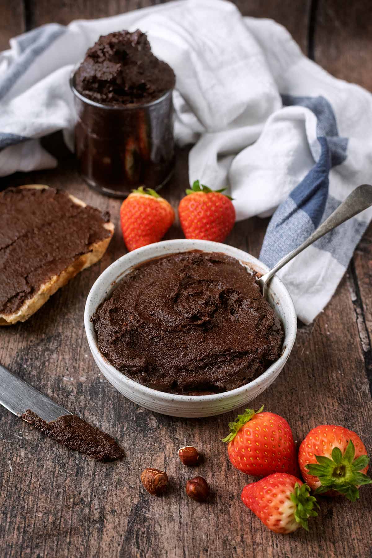 A bowl full of chocolate spread with a jar of the spread in the background.