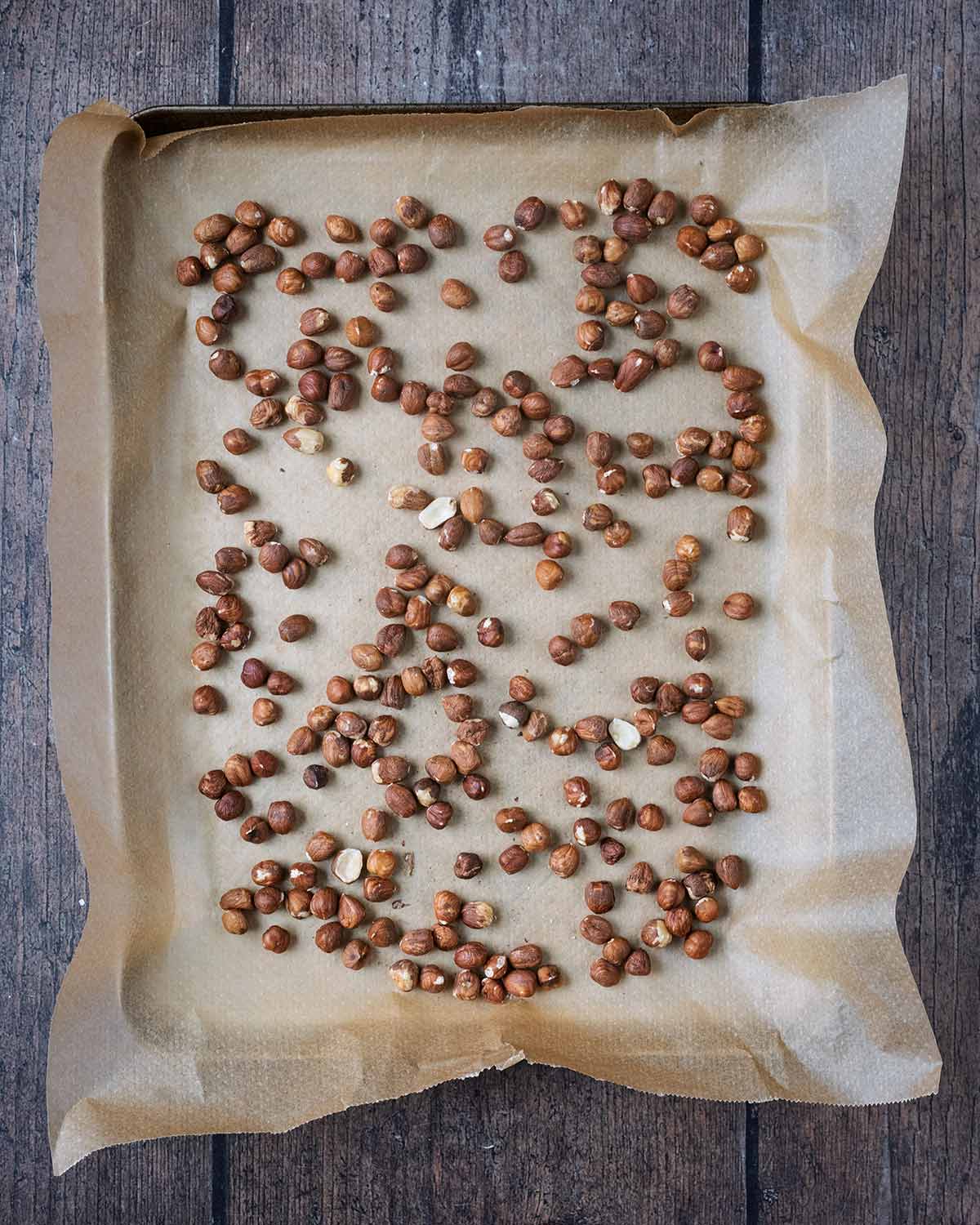 Hazelnuts spread over a lined baking tray.