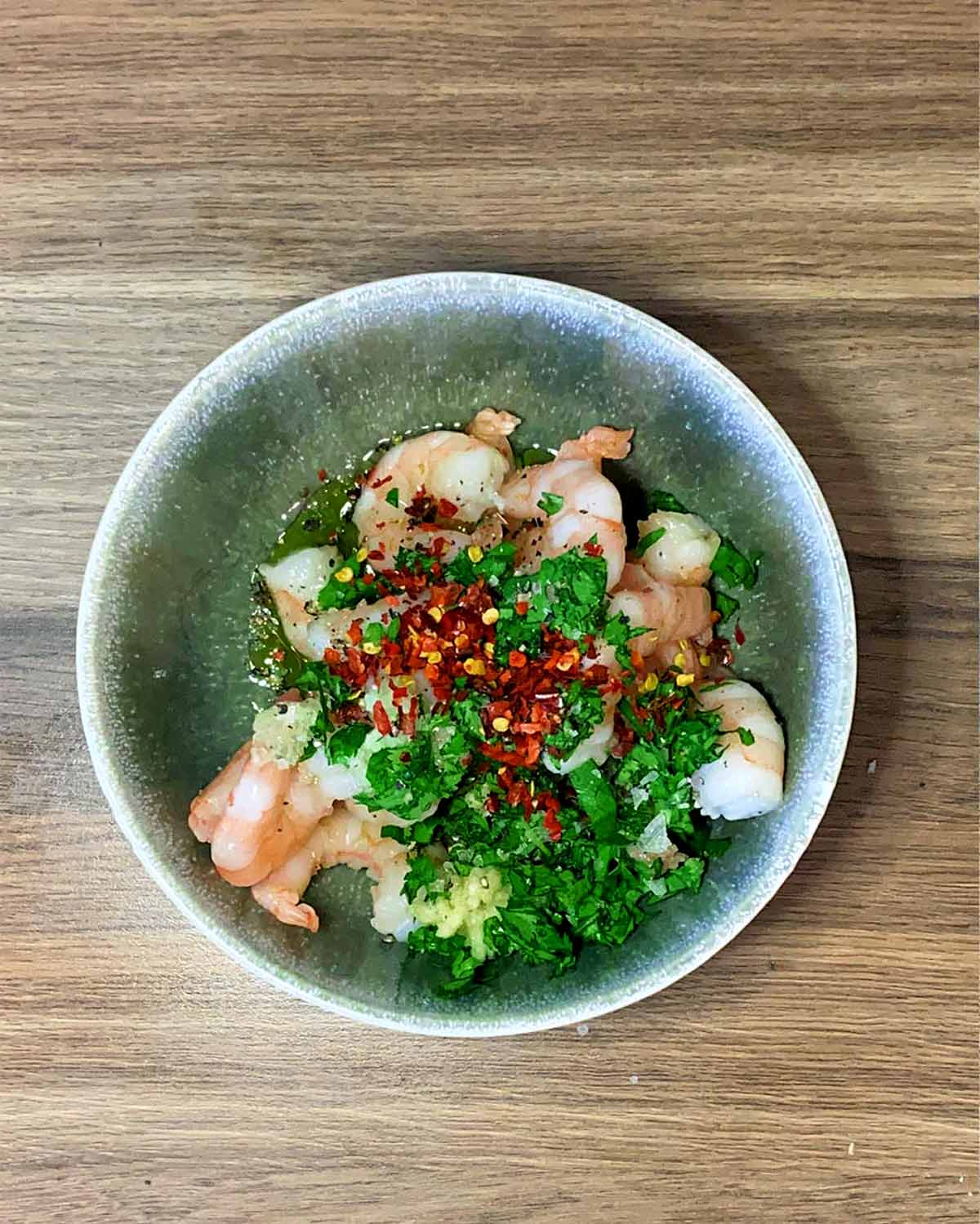 Prawns in a bowl with herbs and chilli flakes.