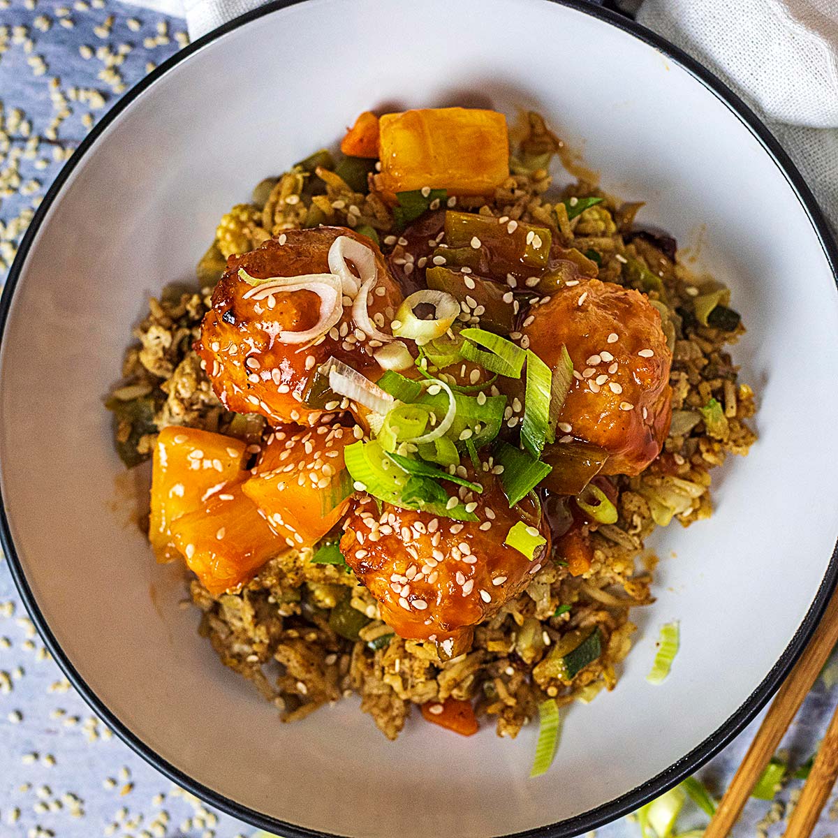 Sweet and sour meatballs in a bowl with rice and chopped spring onions.