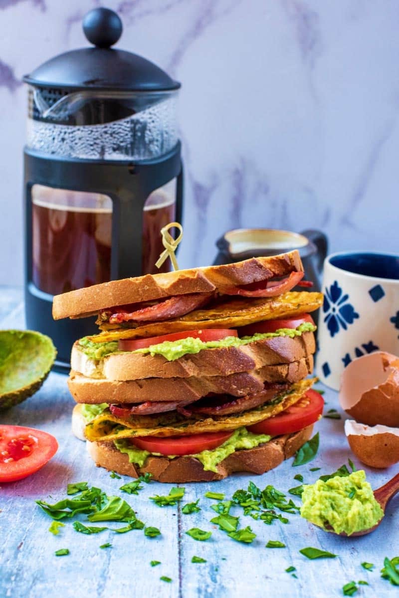 A stack of sandwiches in front of a pot of coffee.