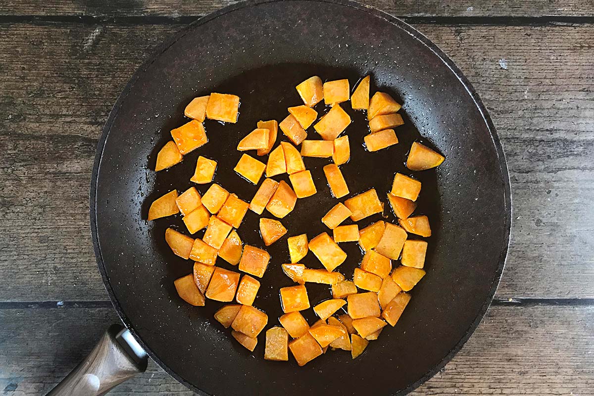 Cubes of sweet potato sautéing in a frying pan.
