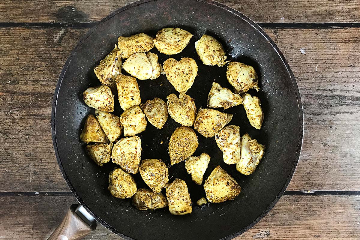 Chunks of spiced chicken cooking in a frying pan.