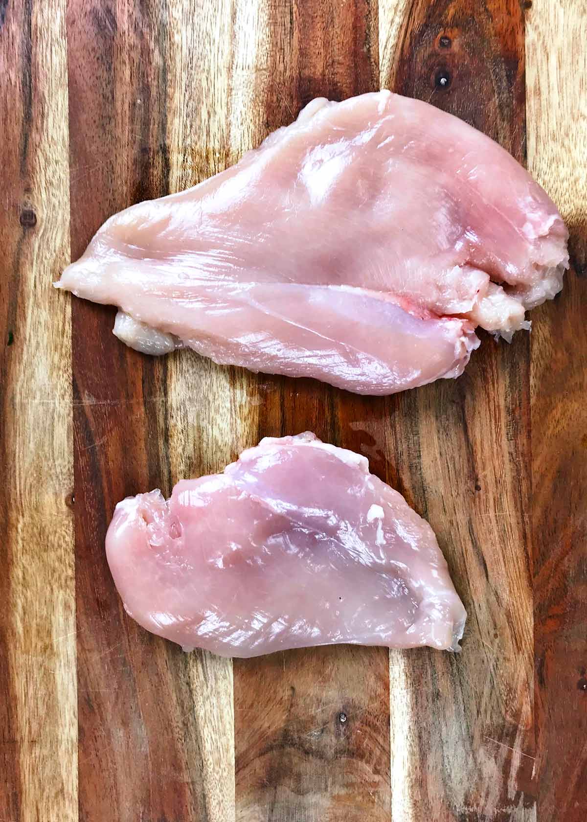 Two flattened chicken breasts on a wooden chopping board.