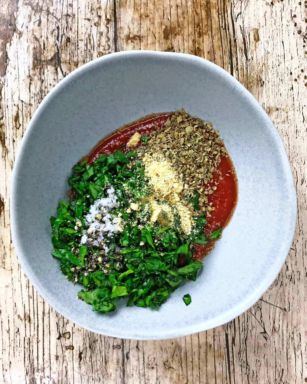 A small bowl containing passata, chopped spinach and dried herbs.