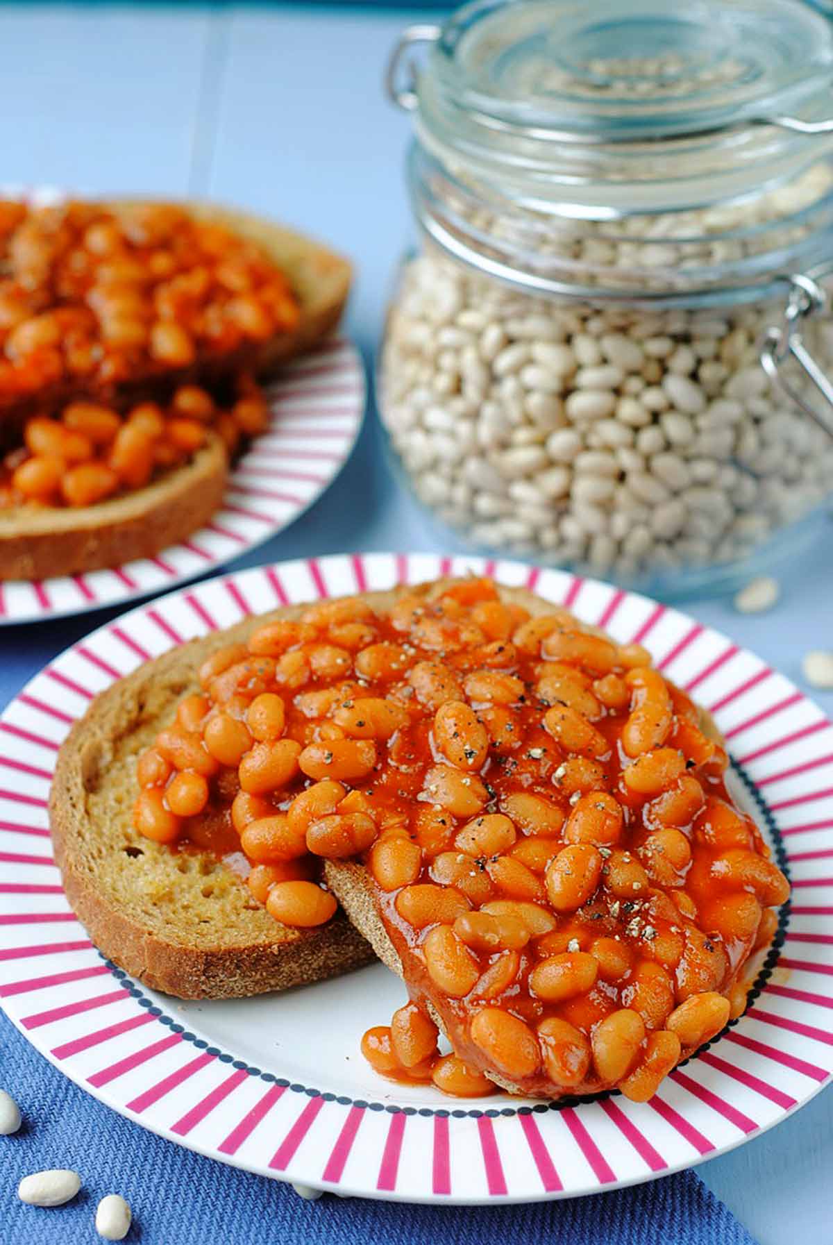 Slow Cooker Baked Beans on a red and white plate in front of a jar of dried beans.