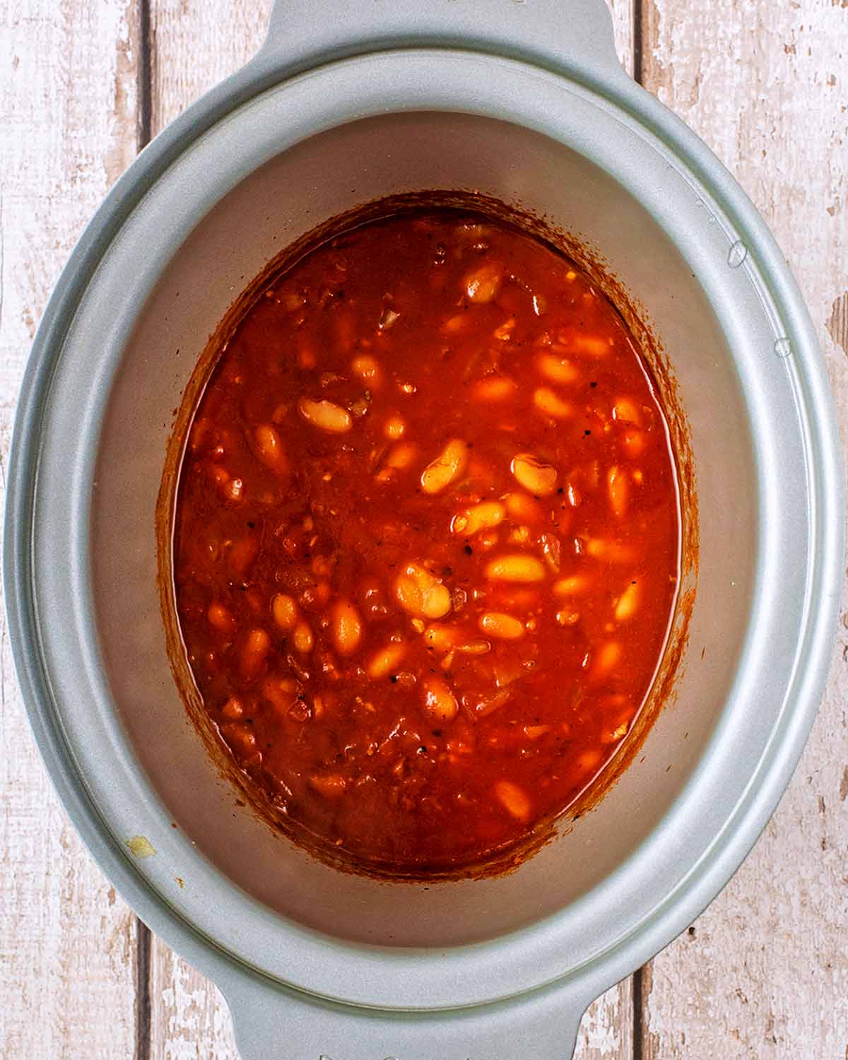 A slow cooker pot containing beans in a tomato sauce.