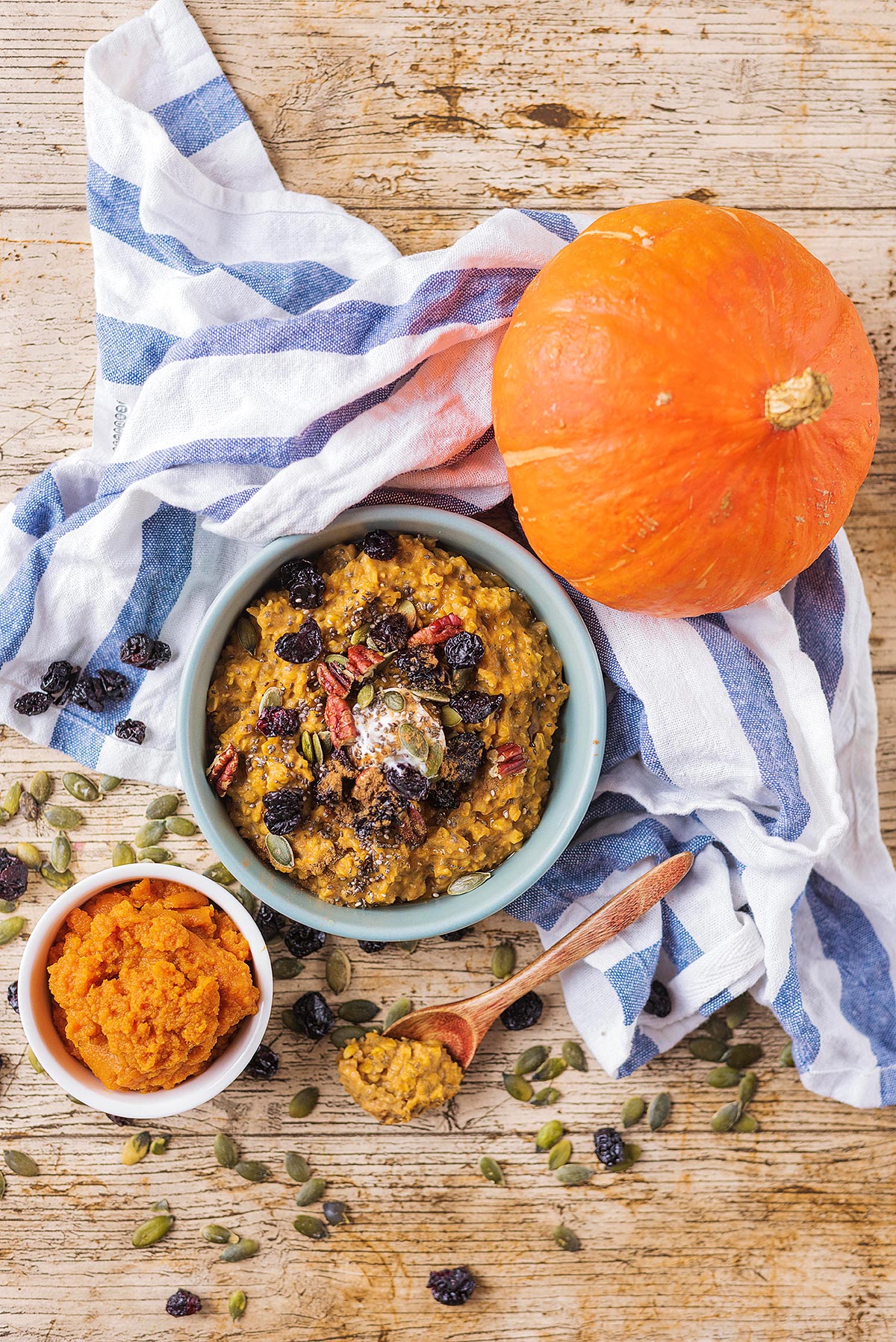 A bowl of porridge next to a smaller bowl of pumpkin puree and a whole pumpkin.
