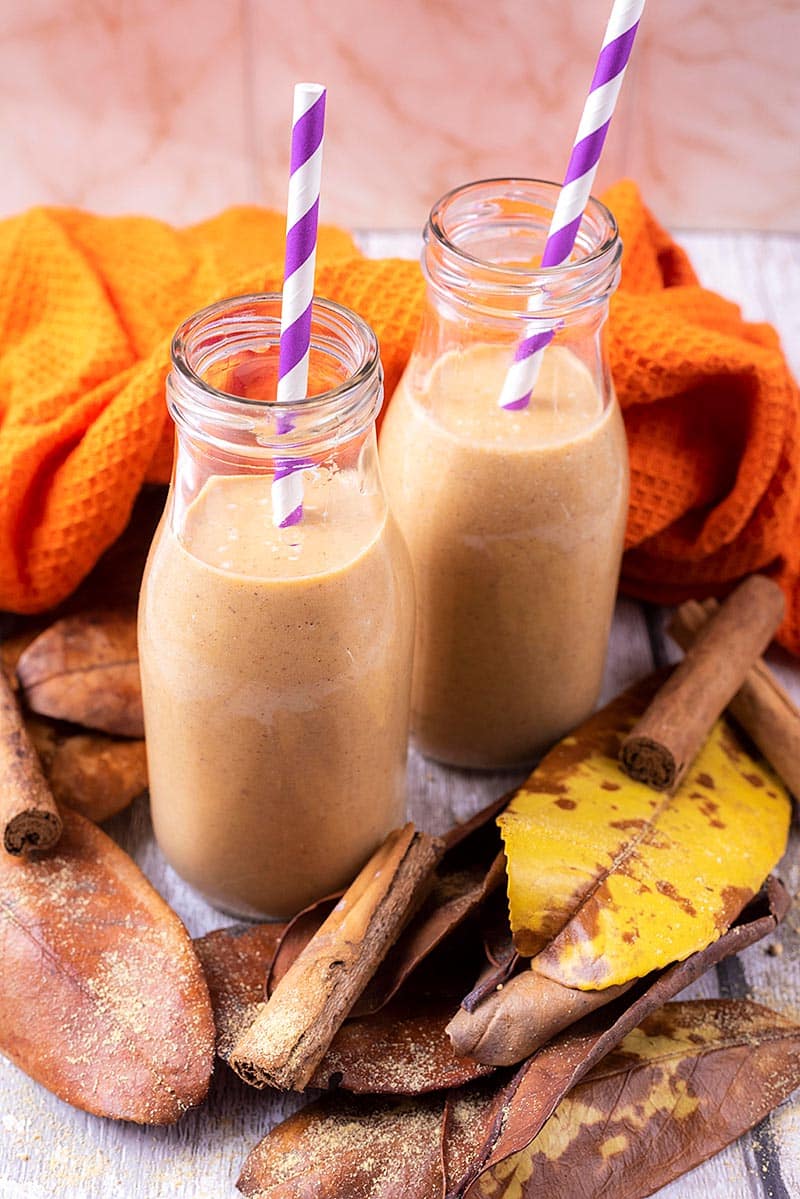 Pumpkin smoothie in two glass bottles surrounded by brown leaves.