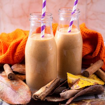 Two glass bottles full of pumpkin smoothie with leaves scattered around them