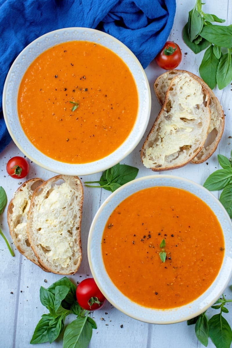 Two bowls of tomato soup with slices of buttered bread and basil leaves.