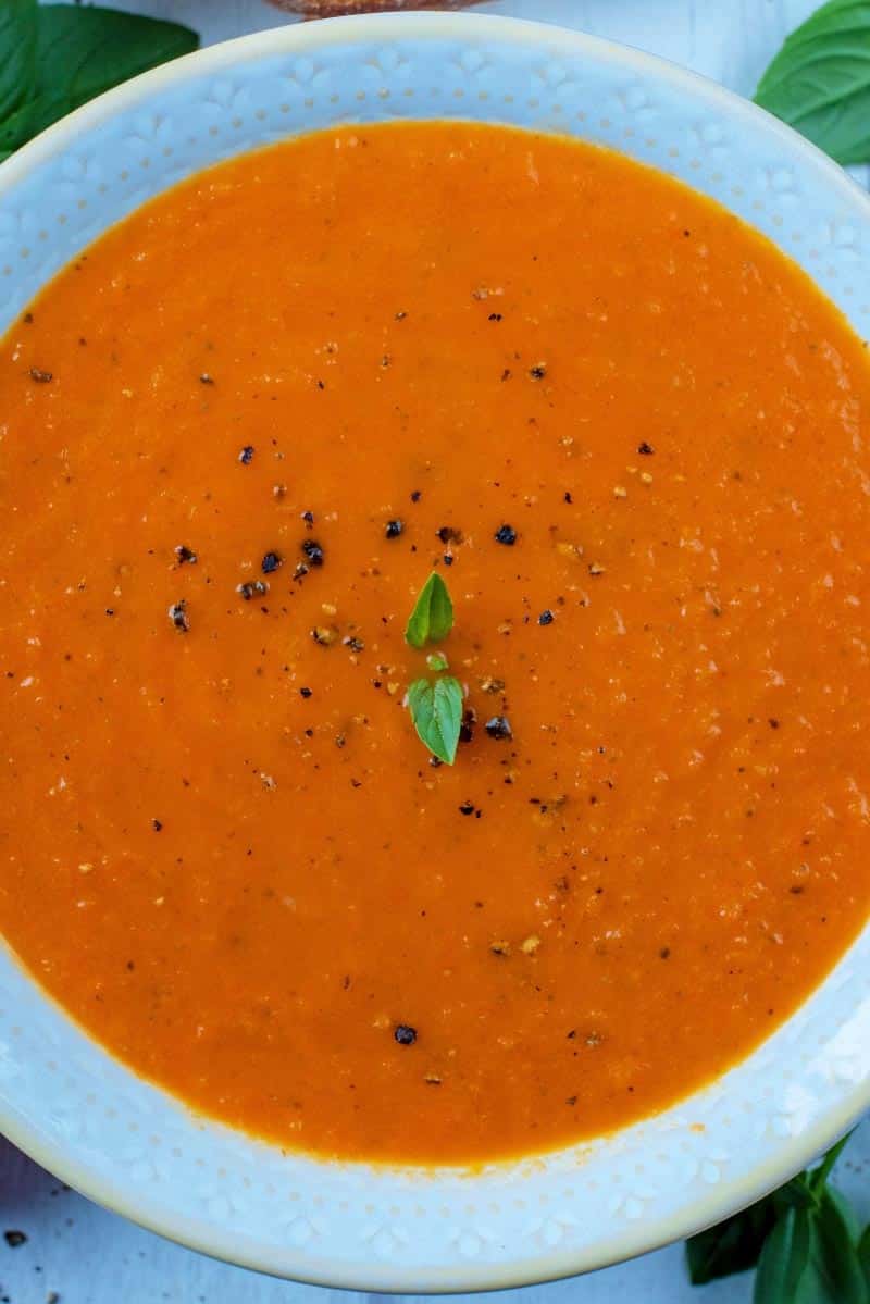 Tomato soup with pepper sprinkled on top and small basil leaves.