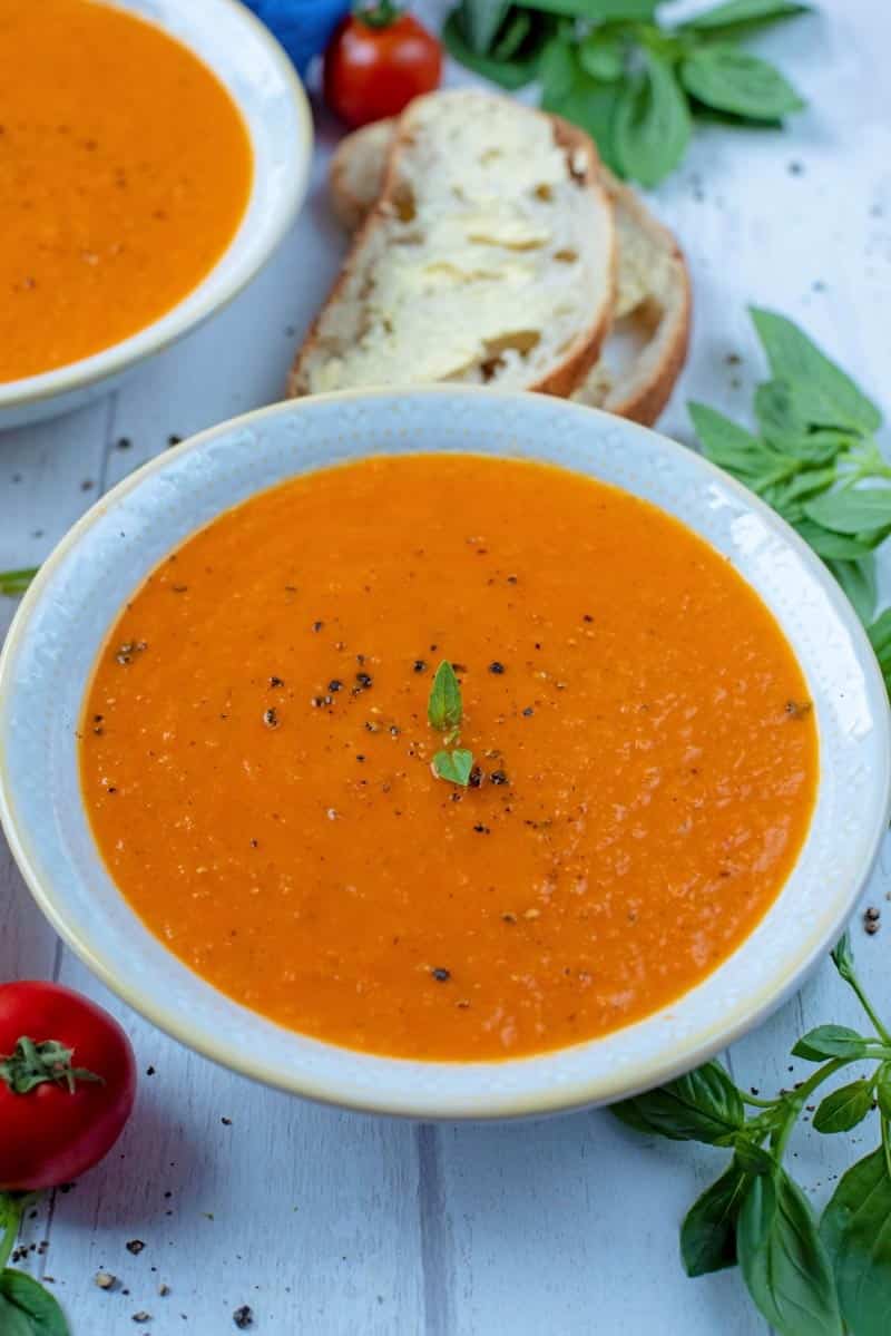 Roasted Red Pepper and Tomato Soup in a blue bowl. Another bowl of soup in the background