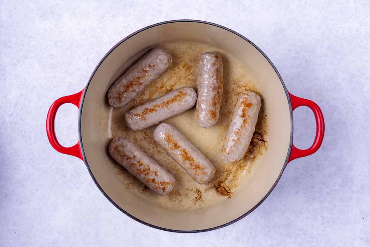 Six sausages cooking in a large pan.