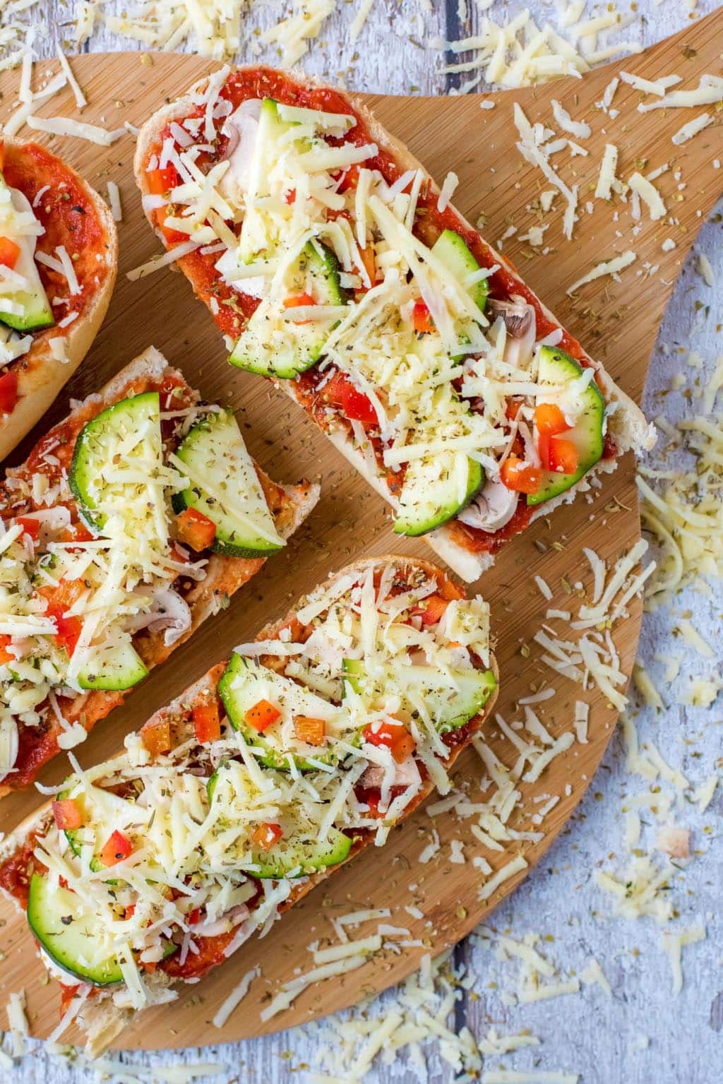 French bread pizzas on a serving board with grated cheese scattered around.