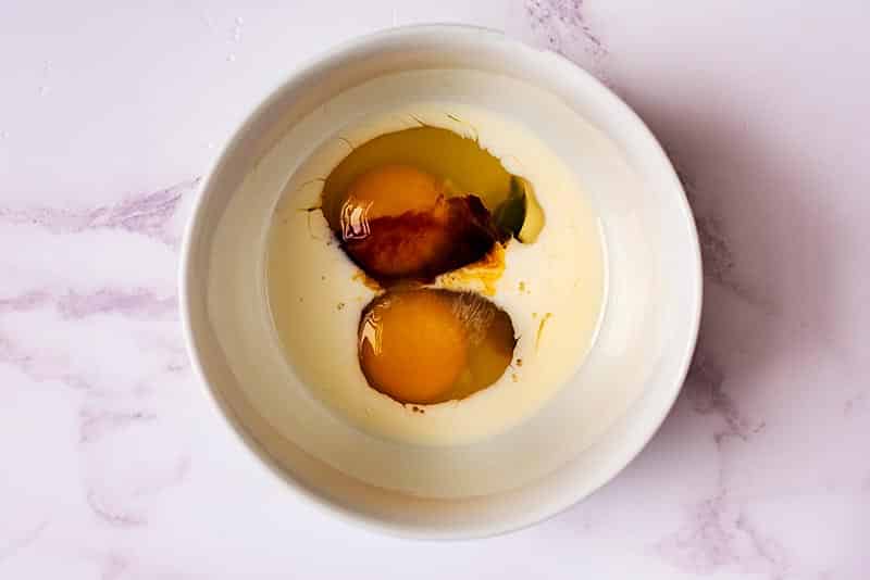 A bowl containing two cracked eggs, milk and some tamari sauce.