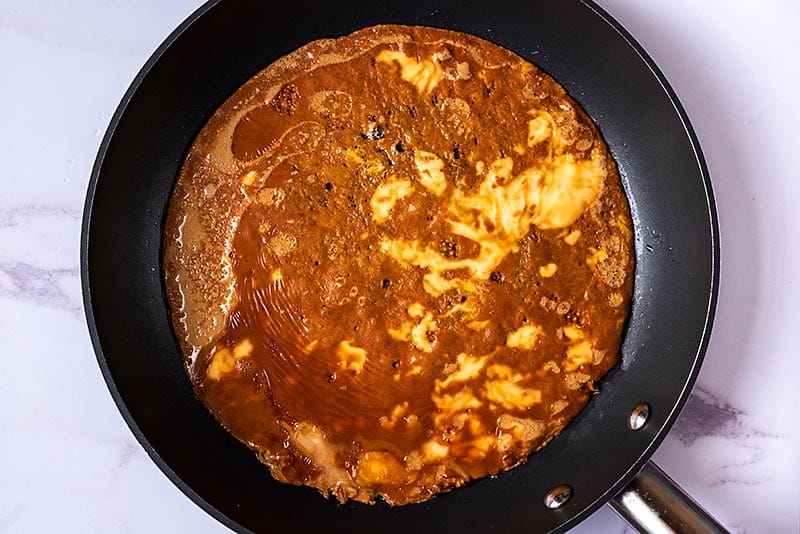 A brown omelette cooking in a frying pan.