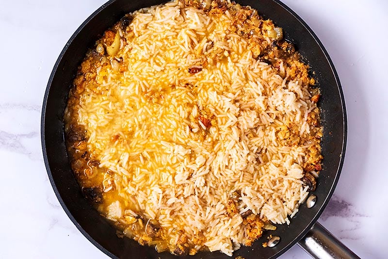 Rice, onions, mushrooms and paste cooking in a frying pan.