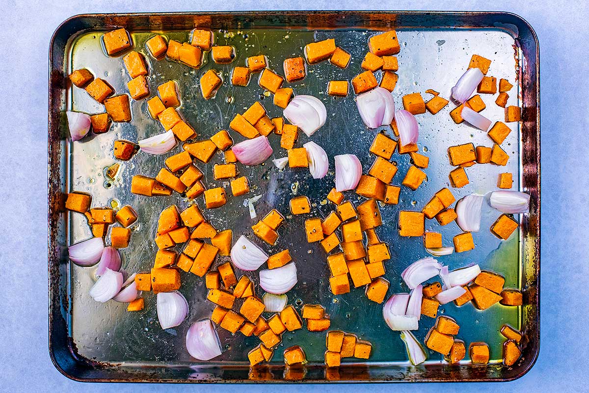 A baking tray covered in cubes of butternut squash and shallots.