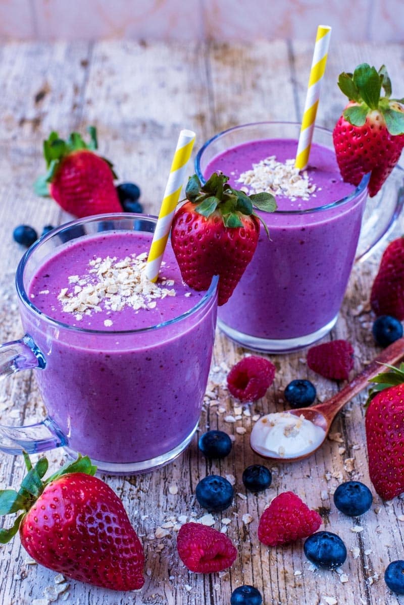 Triple Berry Oat Smoothie in two glasses with straws, oats and strawberries