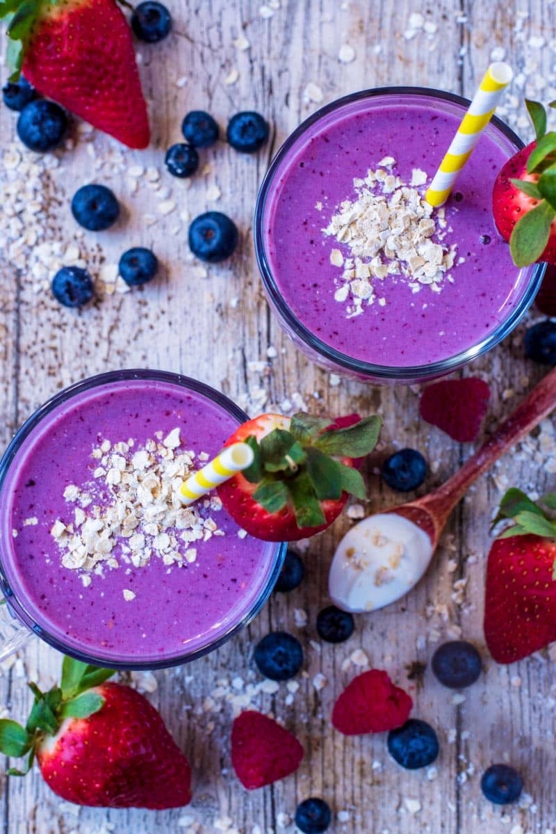 Oats and strawberries on top of two glasses of purple coloured smoothies as viewed from above