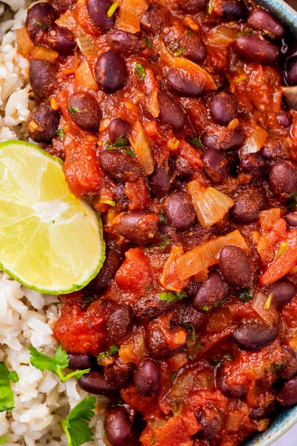 Black beans in a tomato sauce next to some rice with a lime wedge.