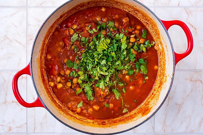 Chickpeas cooing in a tomato sauce with a large pile of cilantro on top.