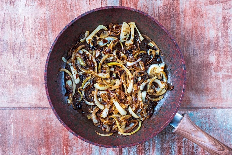 A frying pan with cooked onion slices and chopped mushrooms.