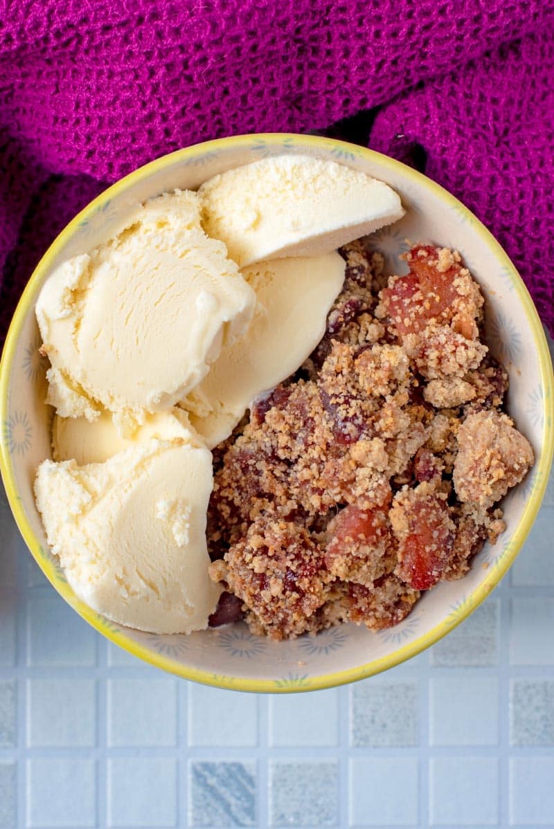 A bowl of crumble and ice cream next to a purple towel.