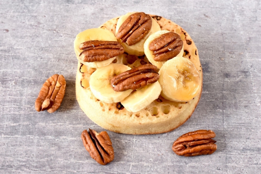 A Crumpet topped with sliced banana, pecans and maple syrup