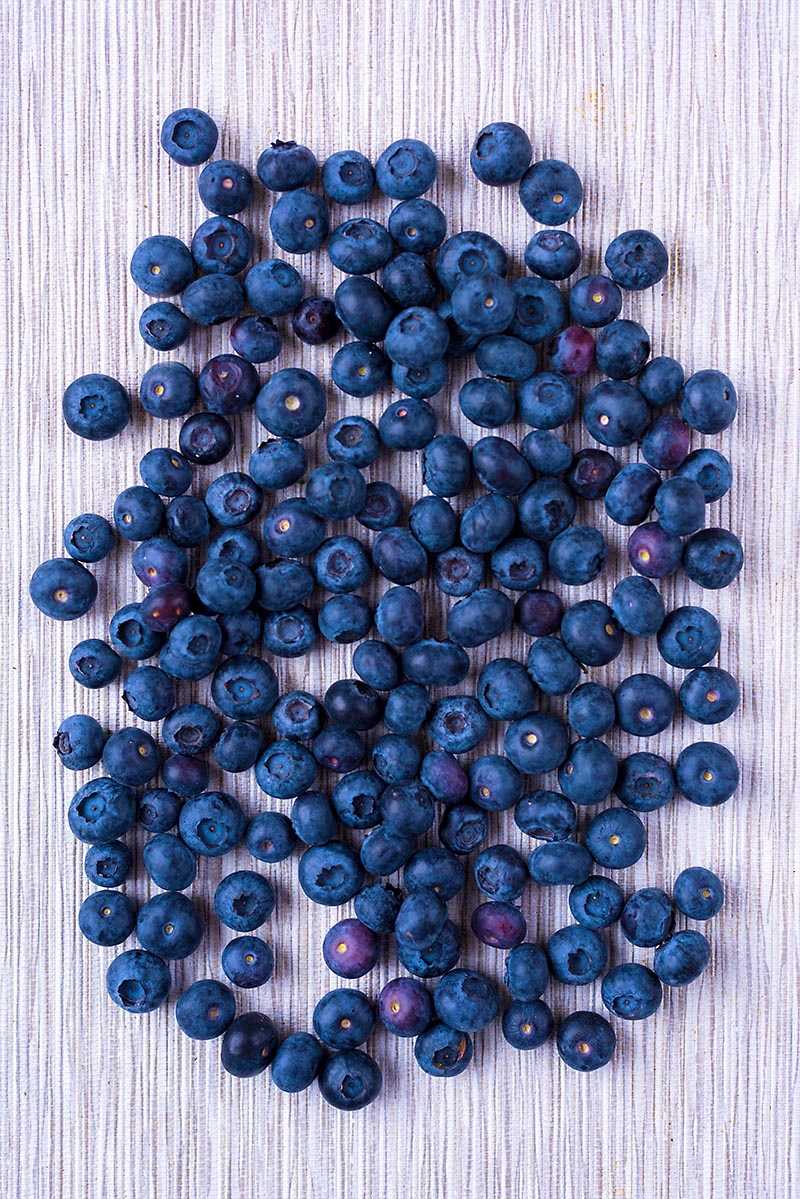 Hundreds of blueberries scattered over a wooden surface.